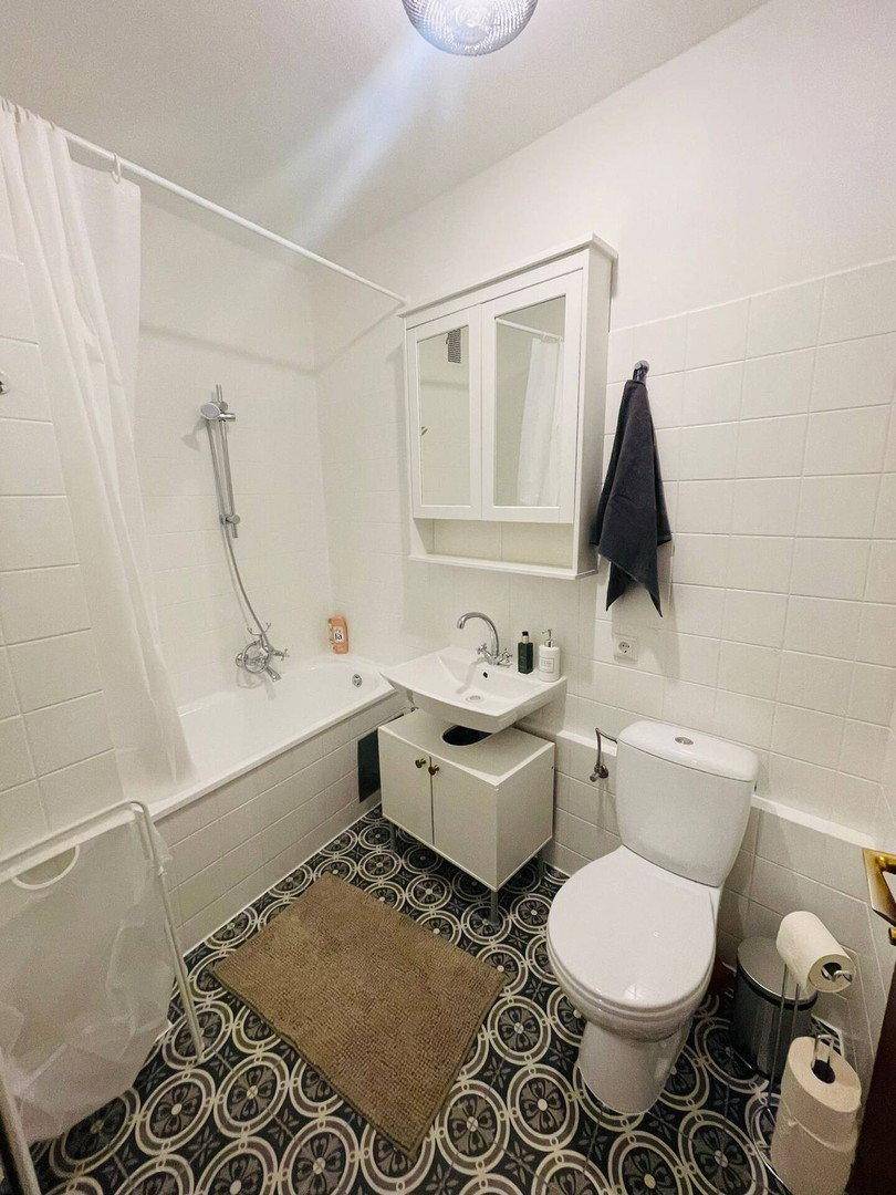 Funktionales Badezimmer mit Badewanne, Waschbecken und Toilette, ausgestattet mit gemusterten Bodenfliesen.