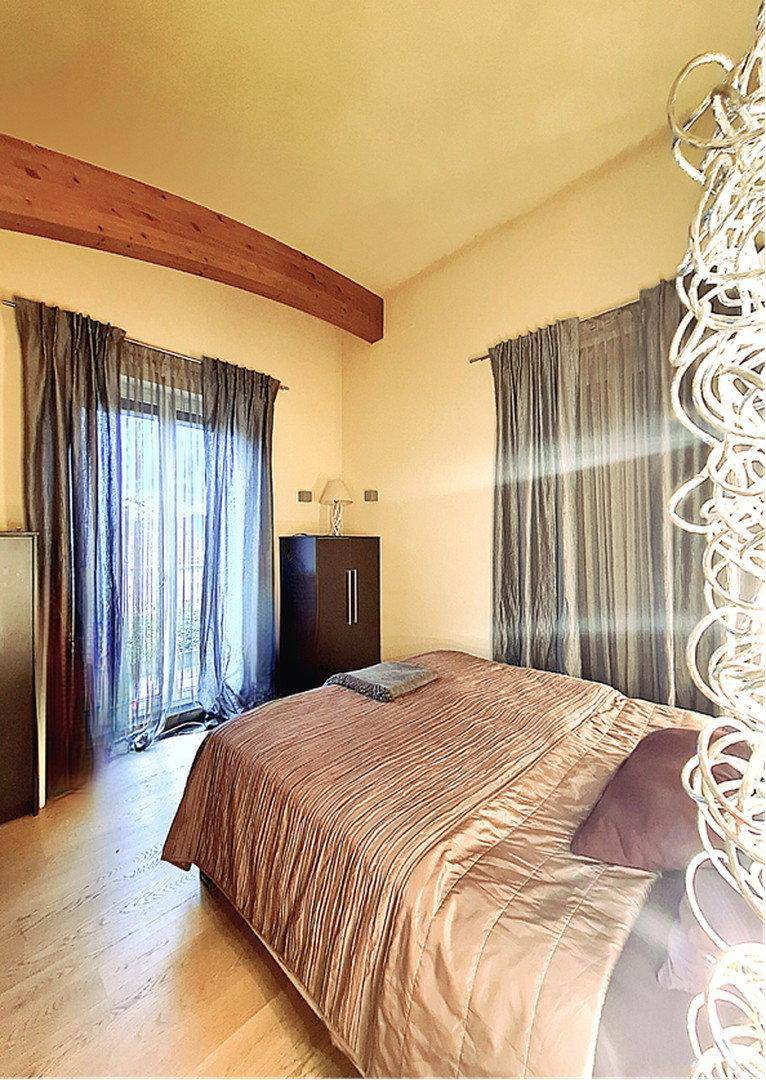 Schlafzimmer mit Holzboden, hohen Decken und Zugang zu einem Balkon.