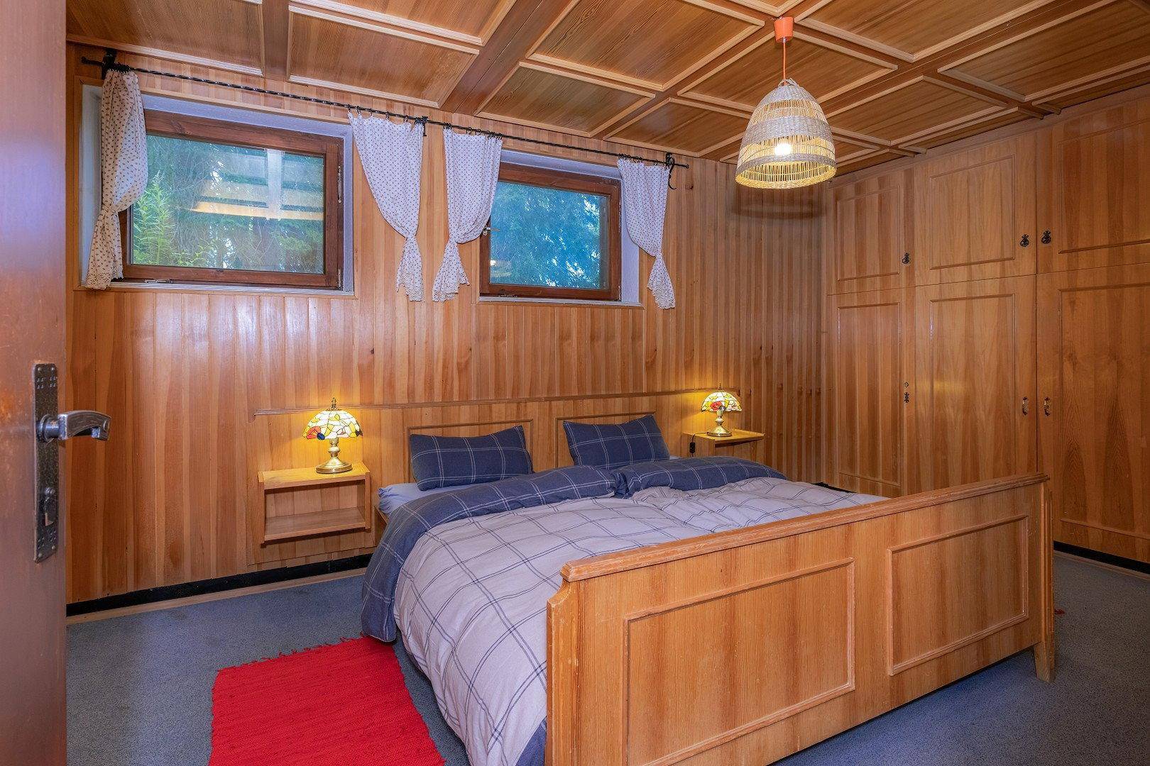 Schlafzimmer im alpinen Stil mit Holzvertäfelung, Doppelbett und zwei kleinen Fenstern.