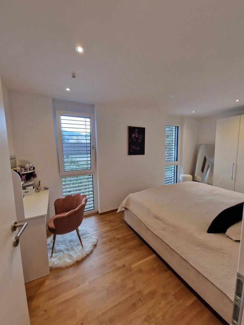 Helles Schlafzimmer mit Holzboden, großem Bett und modernem Schminktisch am Fenster.