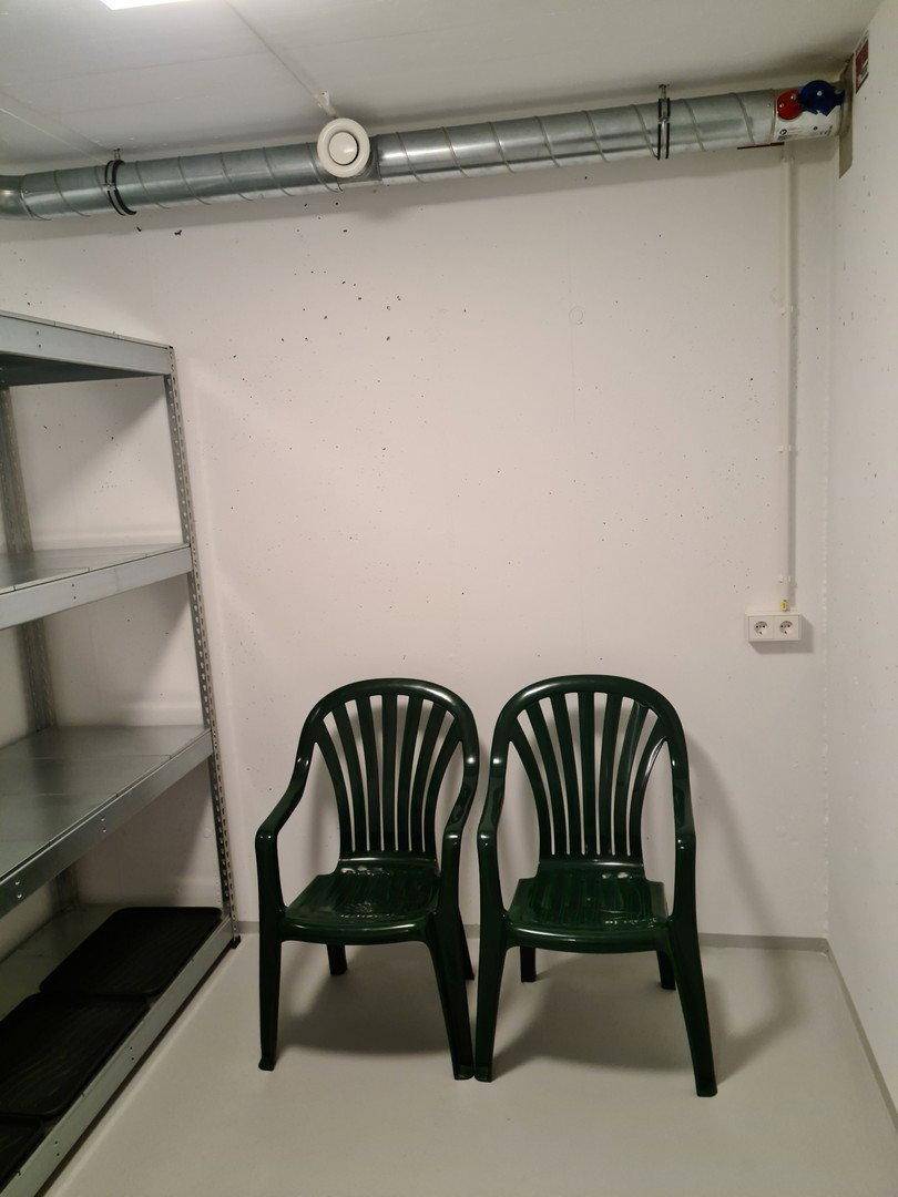 Einfacher Abstellraum mit zwei Plastikstühlen und sichtbaren Lüftungsrohren an der Decke.