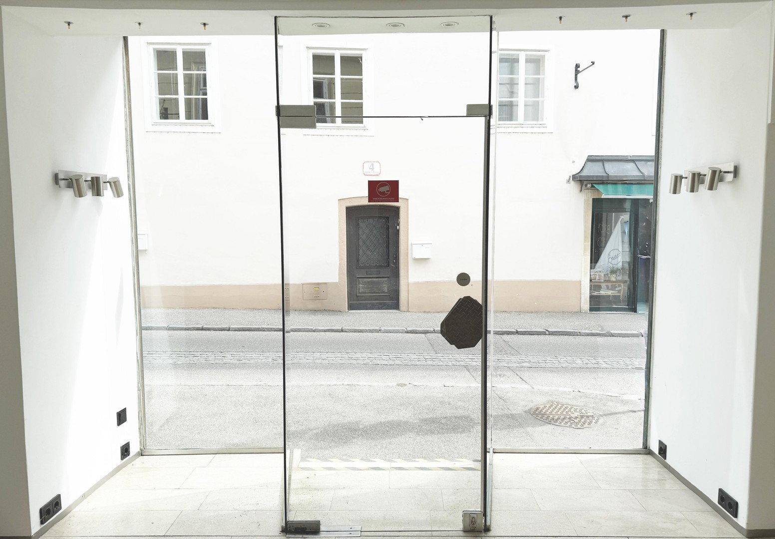 Blick vom Innenraum durch die große Glasfront auf die gegenüberliegende Straßenseite und Gebäude.