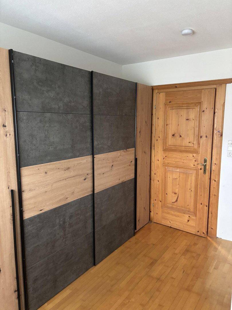 Raum mit einem großen modernen Kleiderschrank aus Holz und grauen Paneelen sowie einer Holztür.