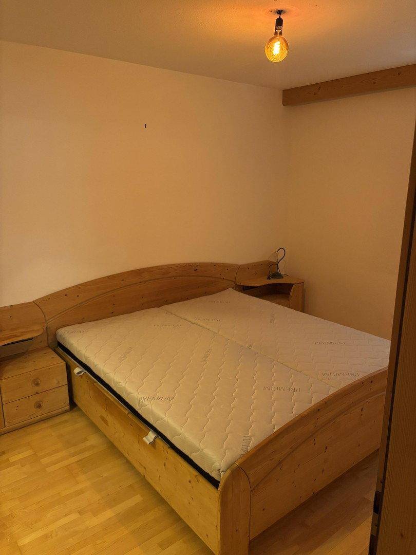 Schlafzimmer mit einem Holzbettrahmen und integrierten Nachttischen, auf hellem Laminatboden.