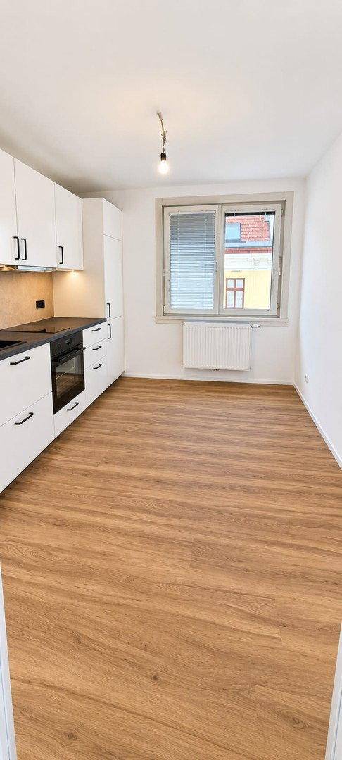 Helle Küche mit weißen Schränken, schwarzer Arbeitsplatte und integriertem Backofen, bereit zur Nutzung.