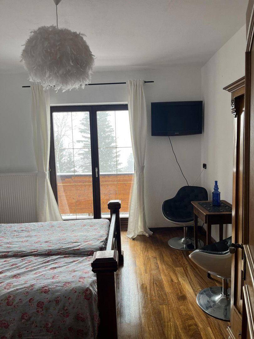 Helles Schlafzimmer mit Doppelbett, Holzboden und Balkontür, die viel Licht hereinlässt.