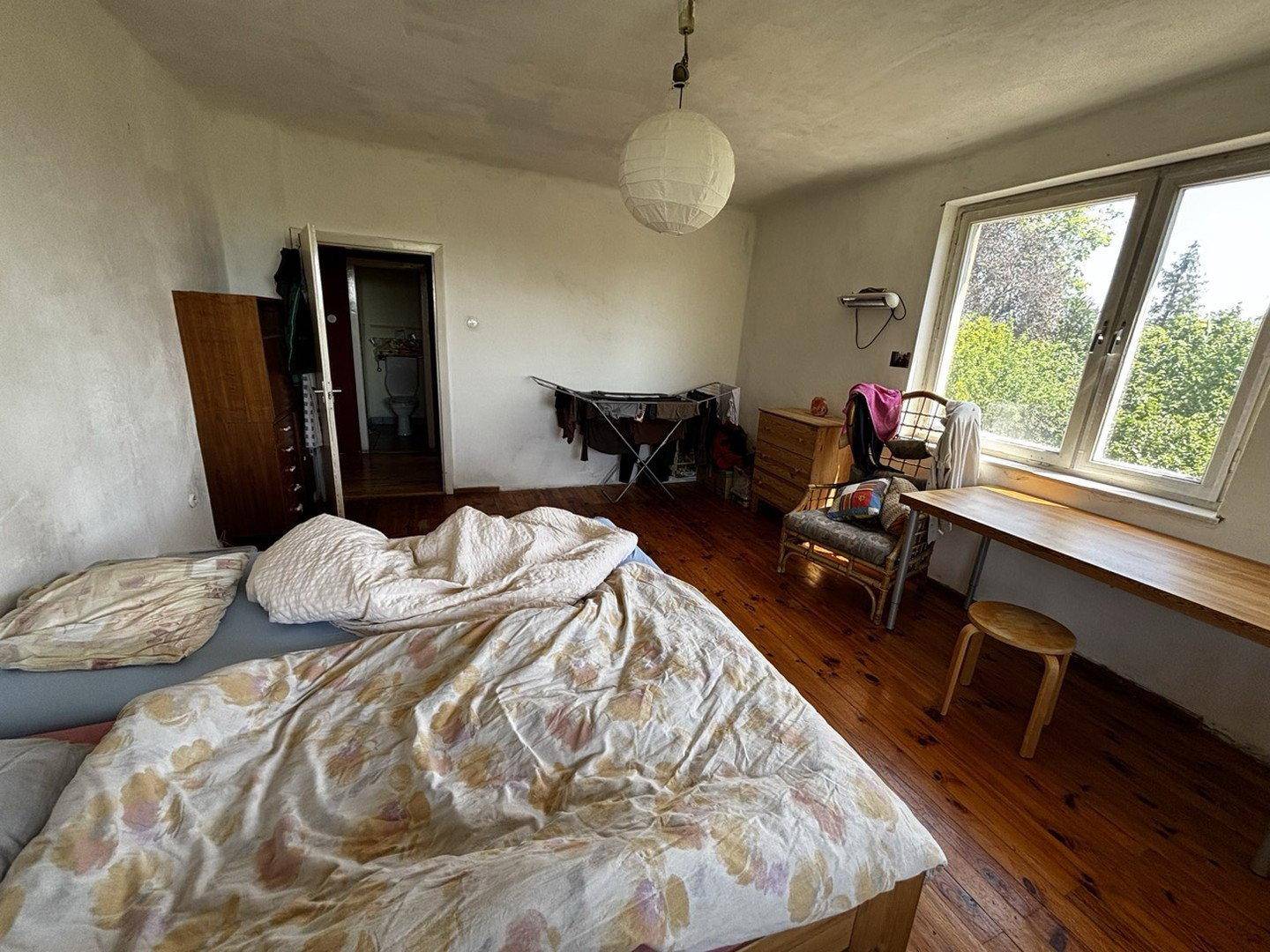 Helles Schlafzimmer mit Holzboden, großem Fenster und Blick ins Grüne.