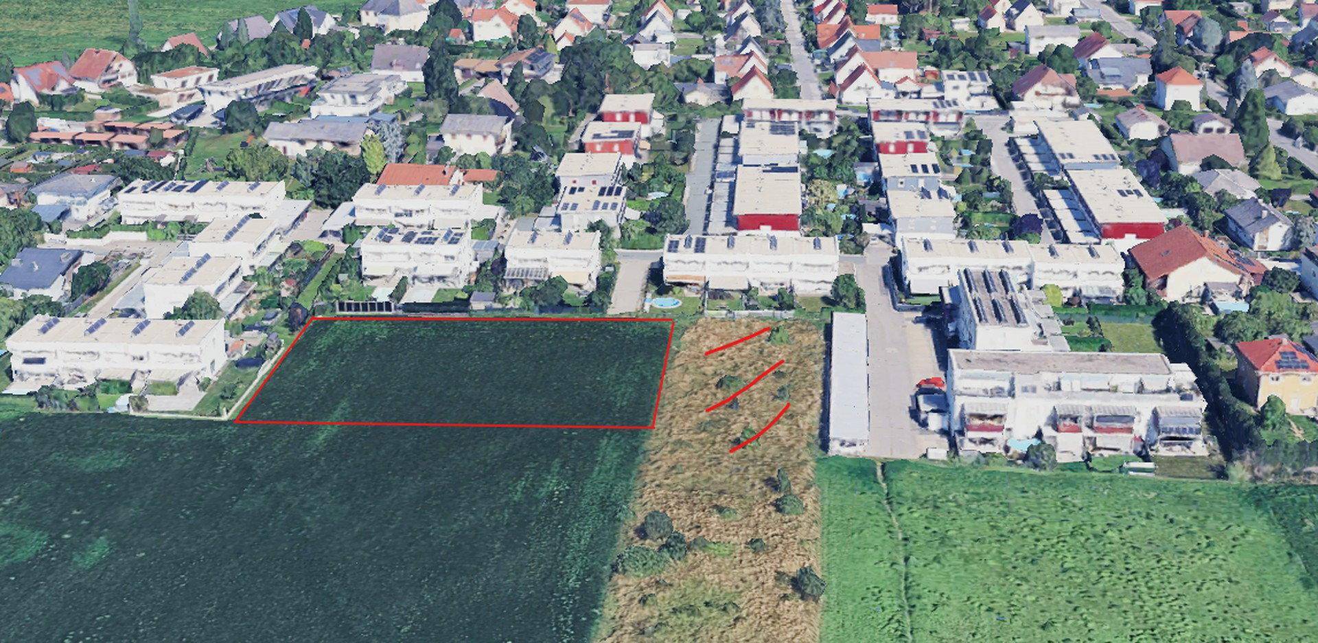 Luftbild einer Wohnsiedlung mit einem großen Feld und einem rot umrandeten Grundstück.