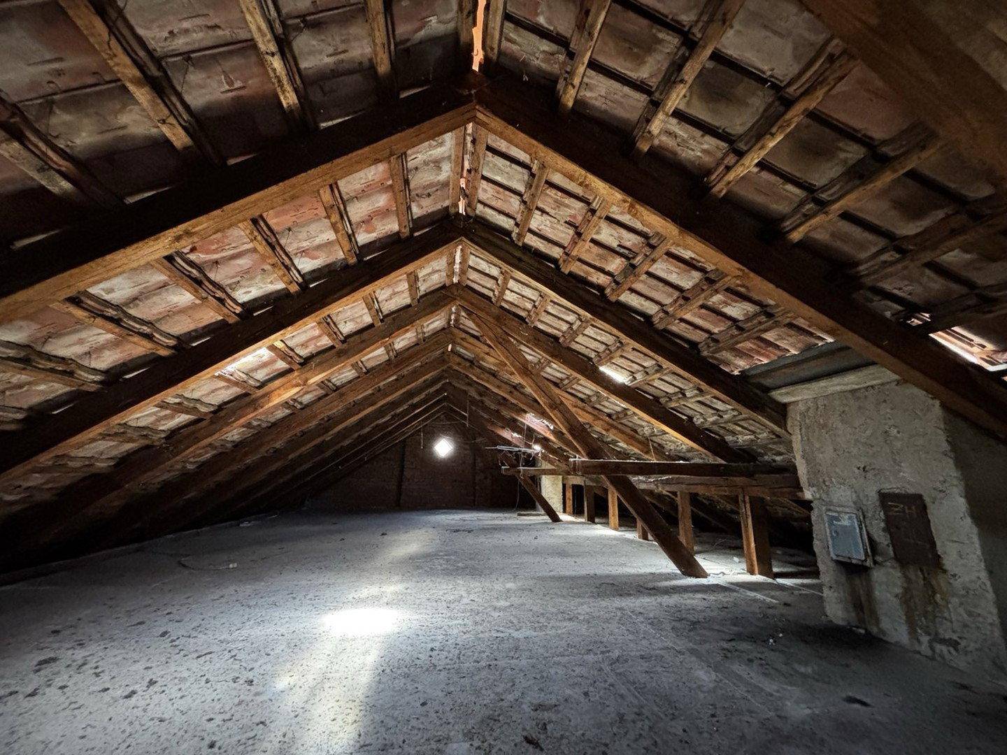 Unausgebauter Dachboden mit sichtbaren Holzbalken und Ziegeln.