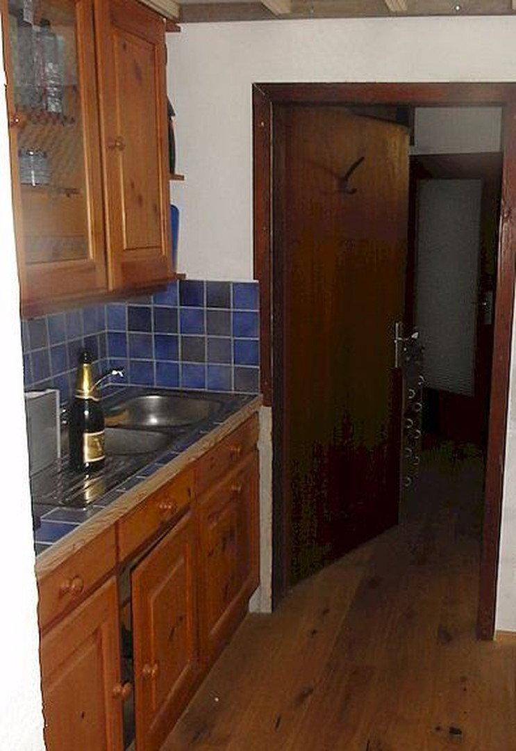 Kleine, funktionale Küchenzeile mit Holzschränken, blauen Fliesen und Spülbecken, ideal für einfache Mahlzeiten.