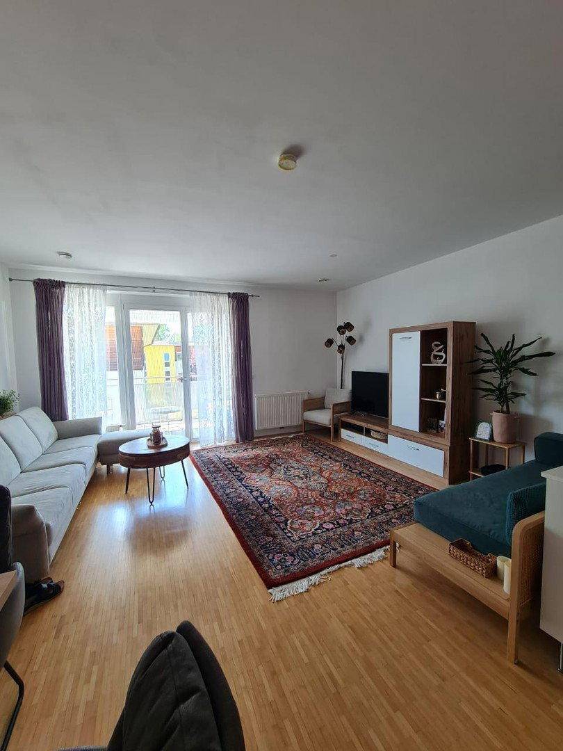 Helles Wohnzimmer mit Parkettboden, gemütlichem Sofa und Zugang zum Balkon.