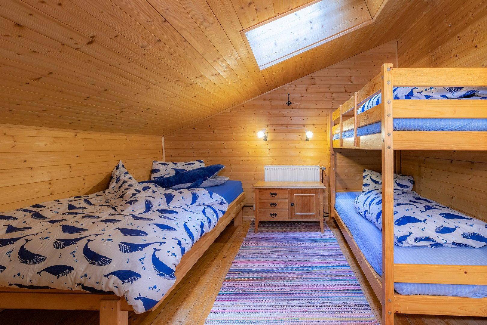 Schlafzimmer mit schräger Holzdecke, Einzel- und Etagenbetten sowie einem Dachfenster.