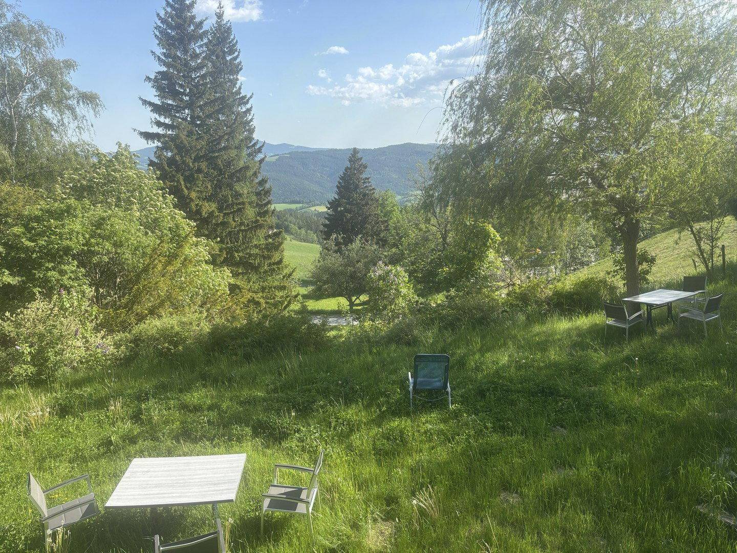 Gartenbereich mit Sitzgelegenheiten und weitem Blick über die hügelige Landschaft und Berge.