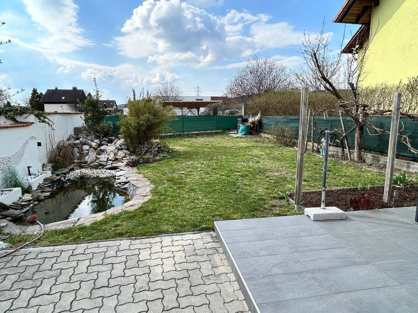 Großer Garten mit Rasenfläche, Zierteich und gepflastertem Bereich für Entspannung.