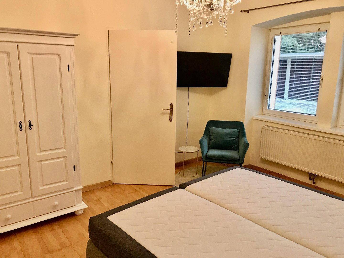 Schlafzimmer mit Bett, Kleiderschrank, Fernseher und Fenster für natürliches Licht.