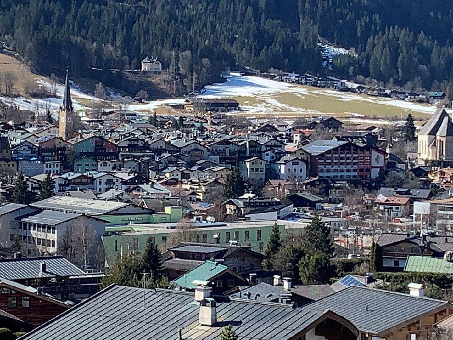 Weitläufiger Blick über ein charmantes Dorf in einem Tal, umgeben von bewaldeten Hügeln und leichtem Schneefall.