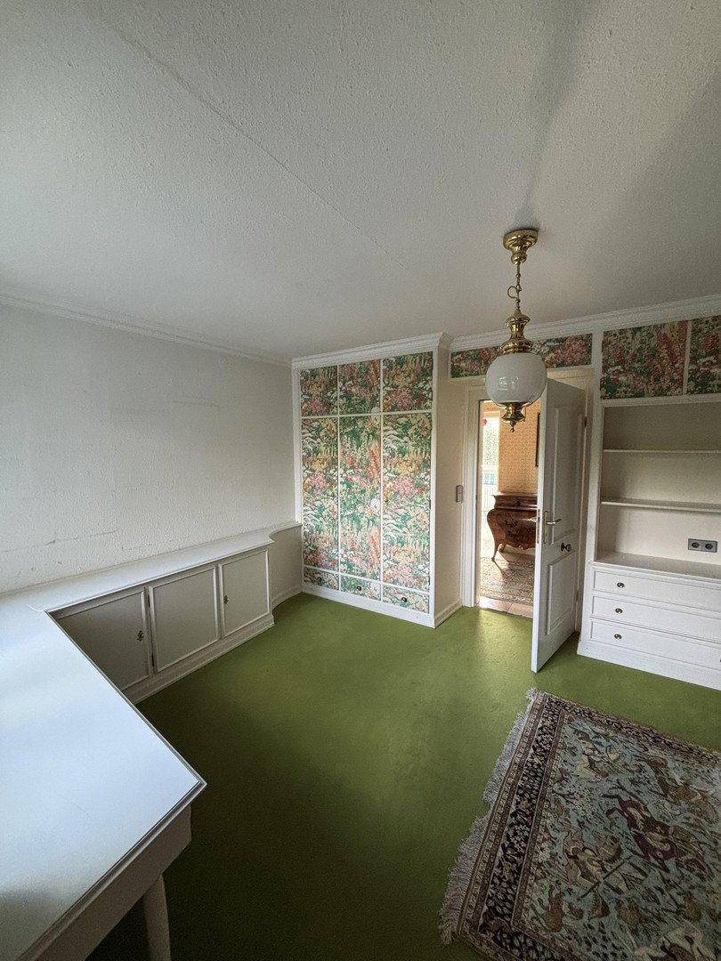 Helles Arbeitszimmer mit grünem Boden, floraler Tapete und integrierten Regalen.