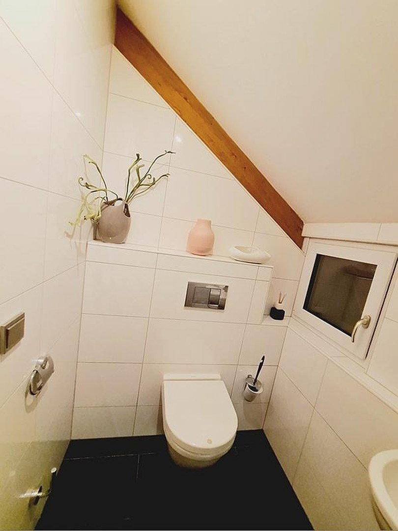 Helles Gäste-WC mit wandhängendem WC, kleinem Fenster und Dachschräge.