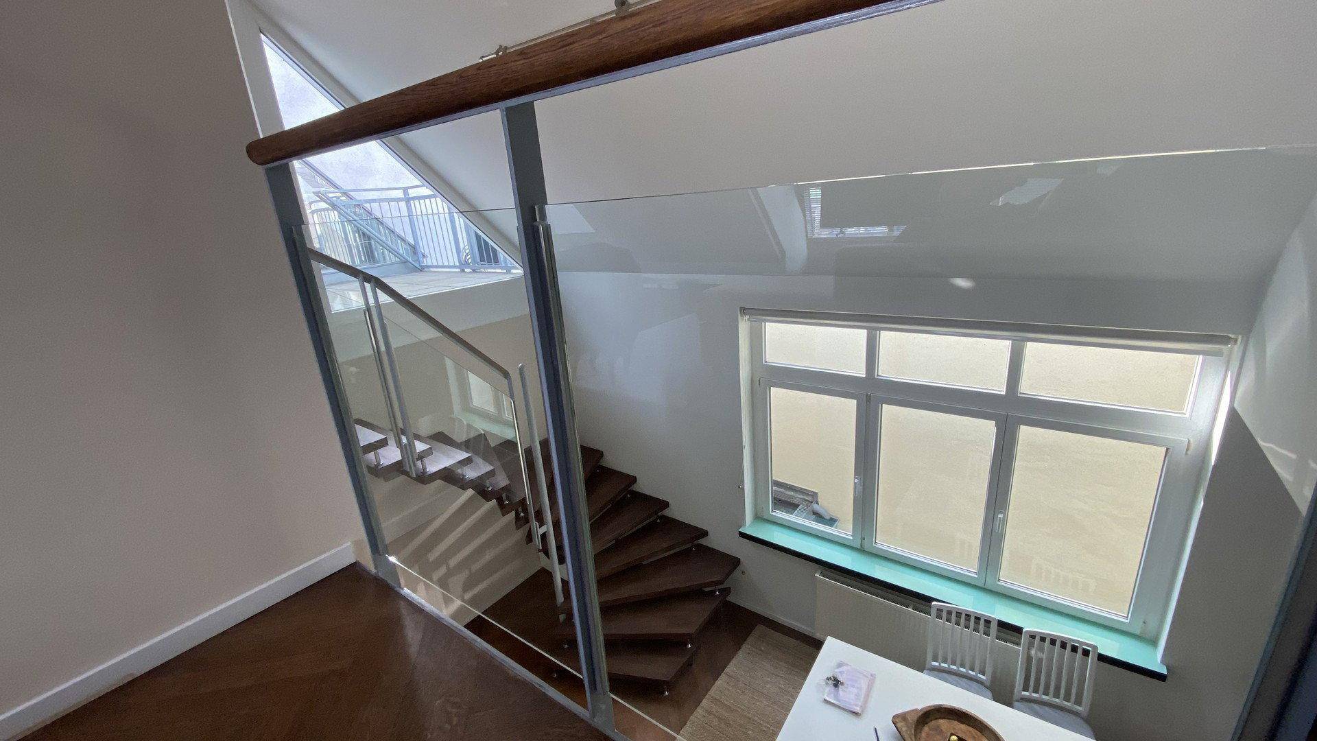 Elegantes Treppenhaus mit Glasgeländer und Holzstufen, das verschiedene Ebenen verbindet.