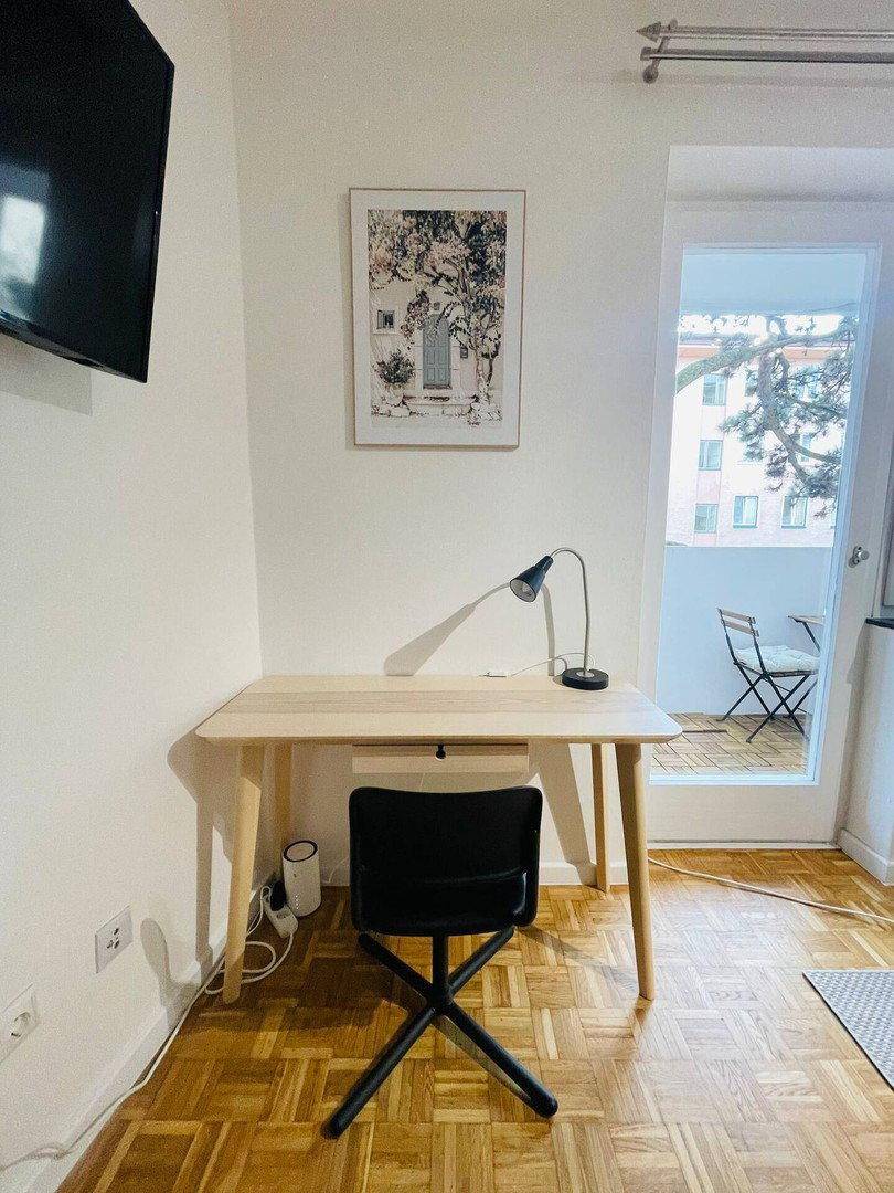 Heller Arbeitsbereich mit Schreibtisch, Stuhl und Zugang zu einem Balkon.