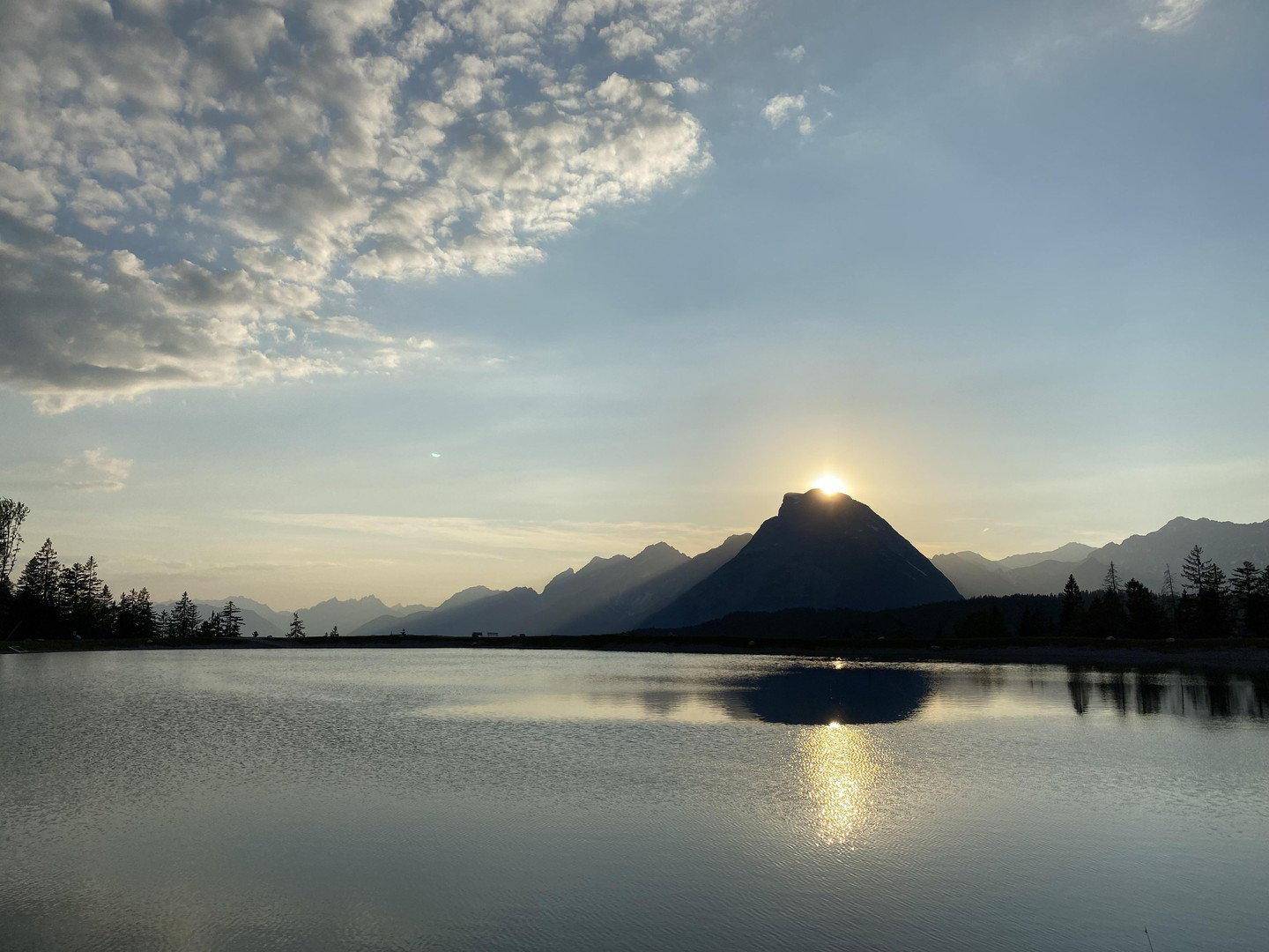 Malerischer Sonnenuntergang über einem See mit Bergkulisse im Hintergrund.