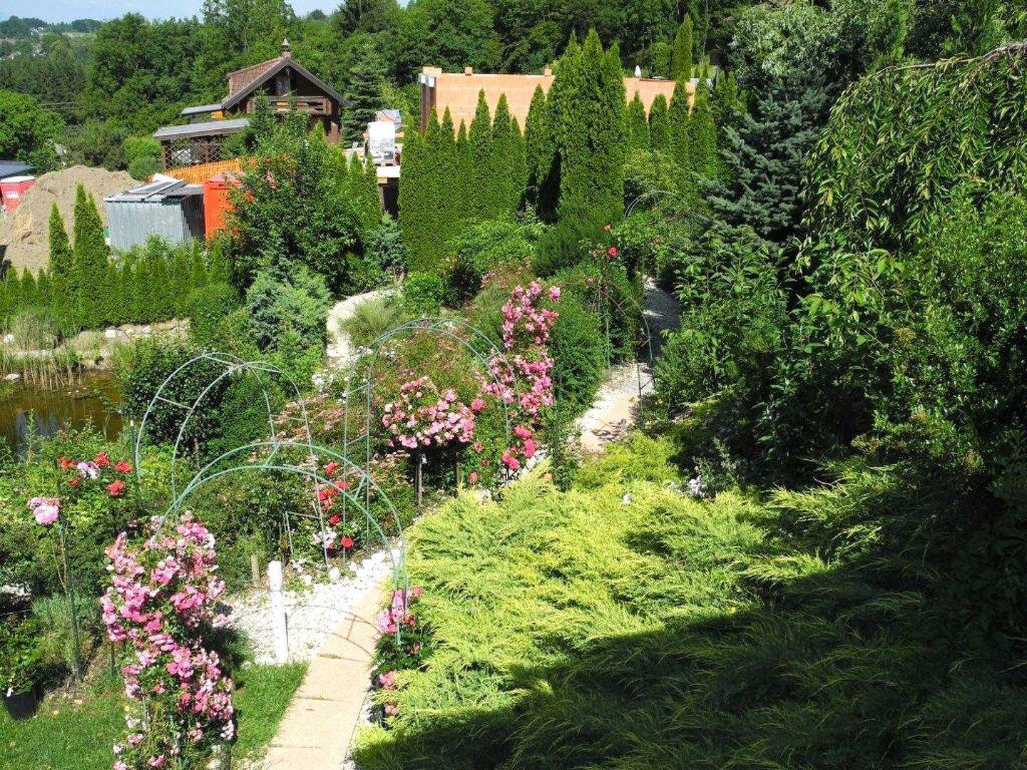 Üppiger, terrassierter Garten mit Blumenbeeten, Wegen und Teich in ländlicher Umgebung.