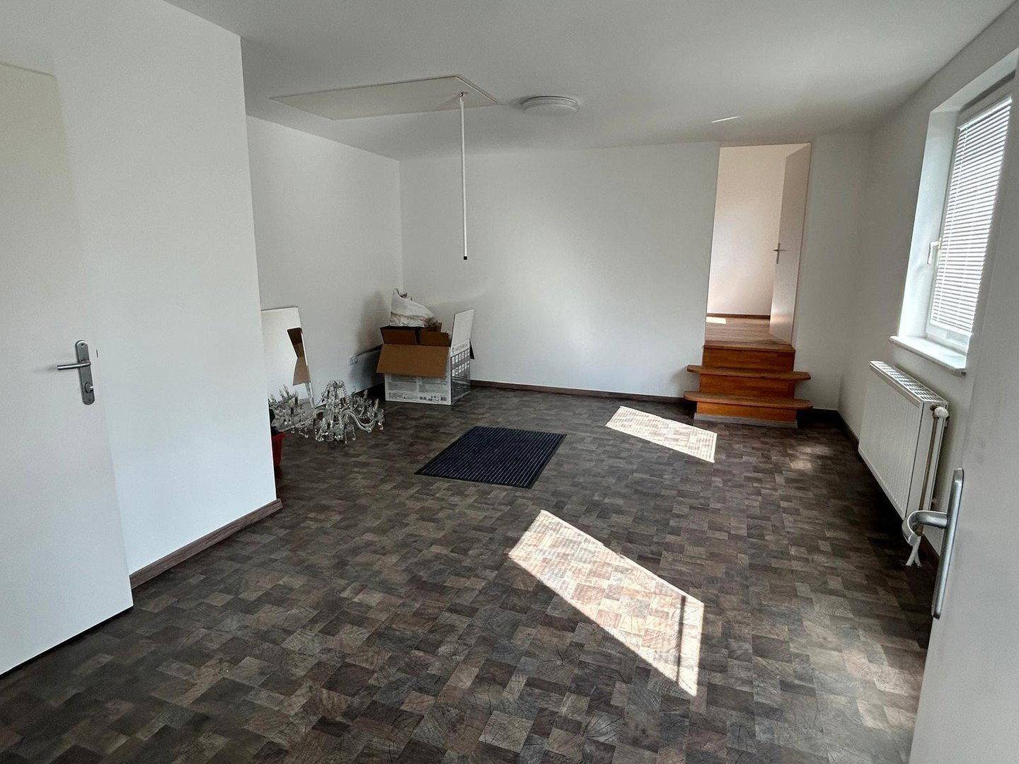 Helles Wohnzimmer mit dunklem Fliesenboden und Zugang zu einem Dachboden über eine Leiter.