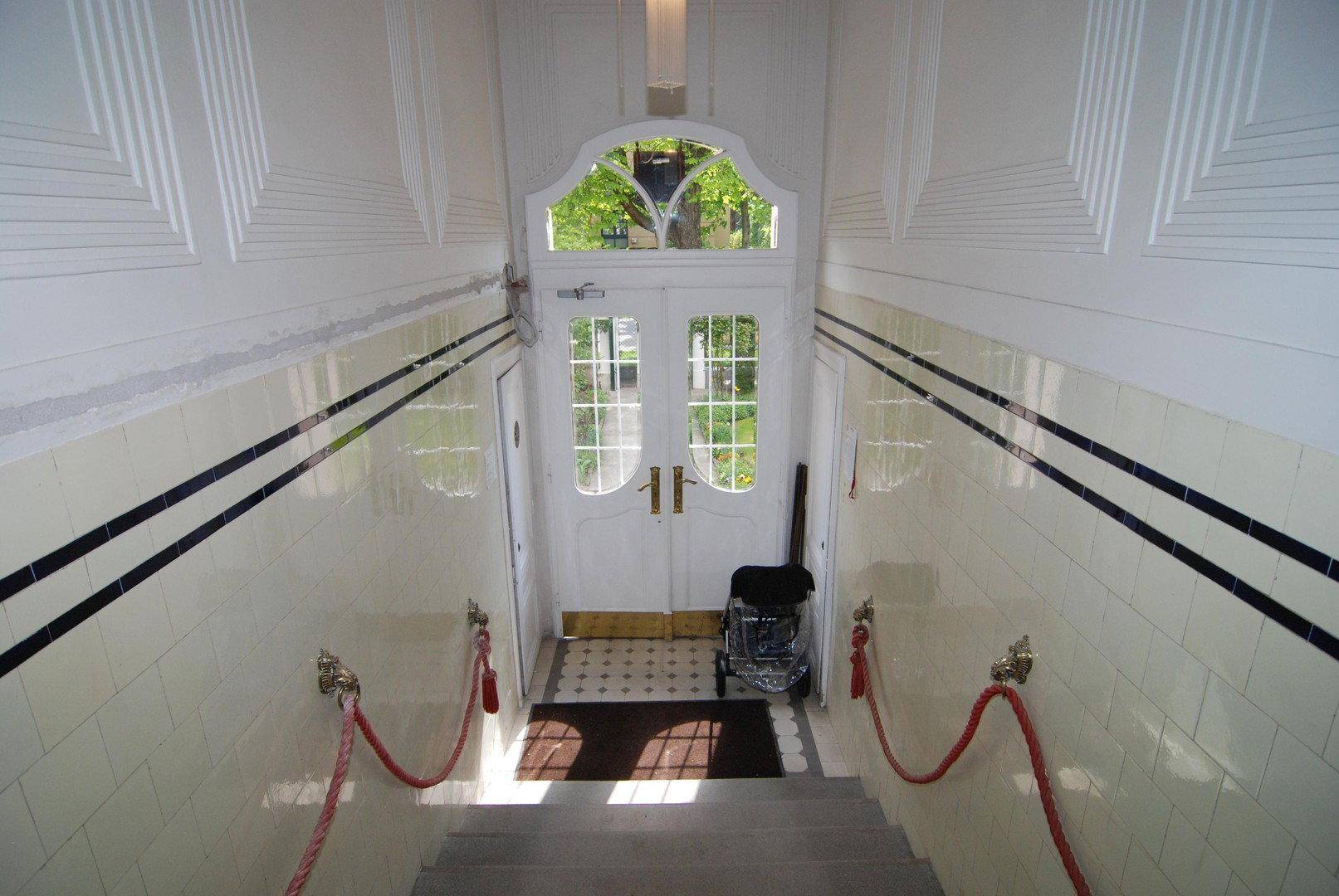 Eingangsbereich mit Doppeltür, dekorativen Fliesen und Treppe, die zum Haupttreppenhaus führt.