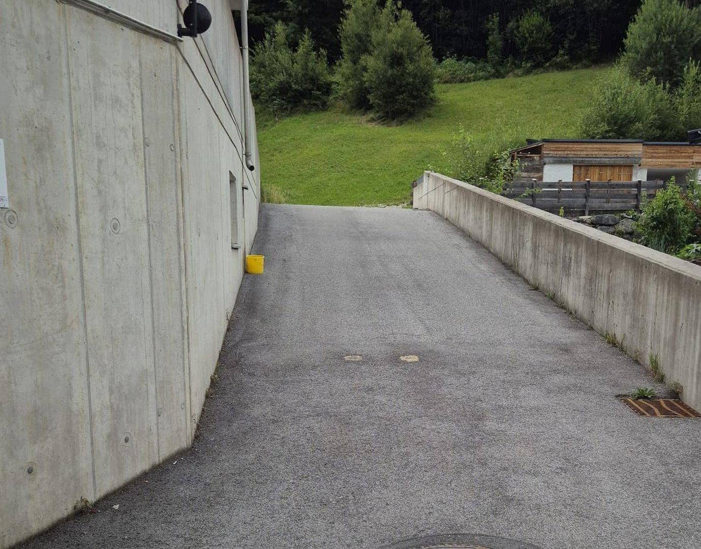Zufahrtsrampe aus Beton zu einer Tiefgarage, umgeben von Grünflächen.