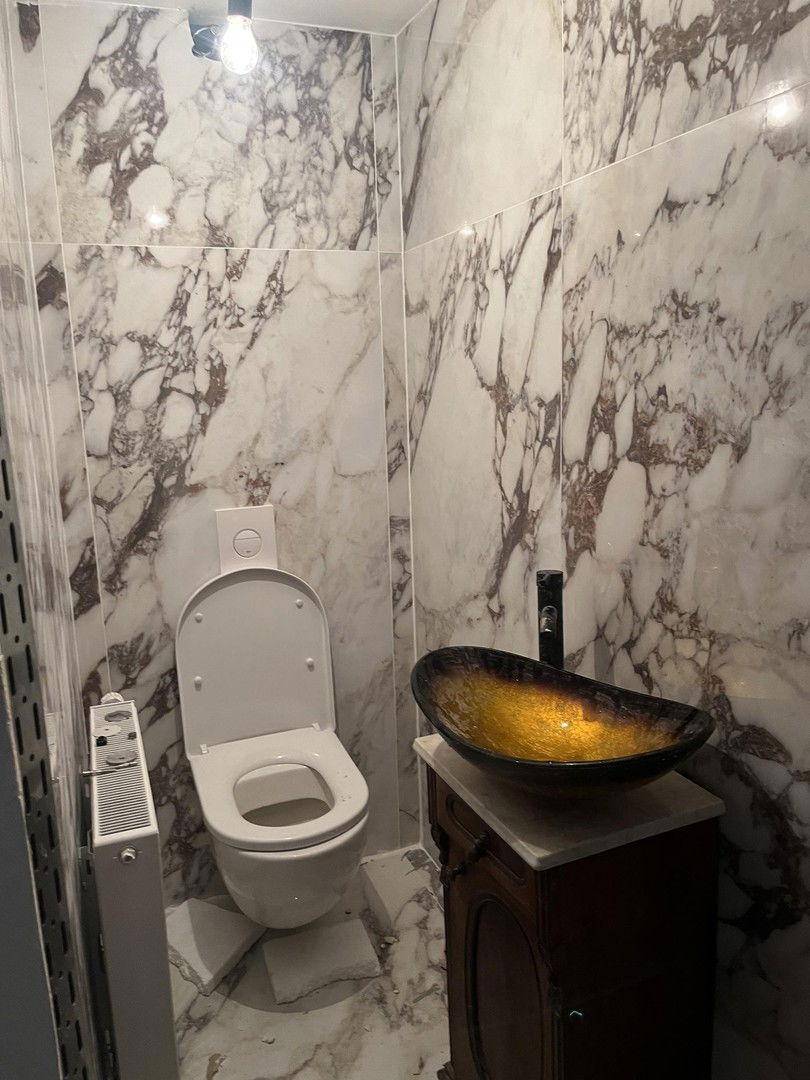 Kleines WC mit Marmorfliesen, wandmontierter Toilette und modernem Aufsatzwaschbecken.