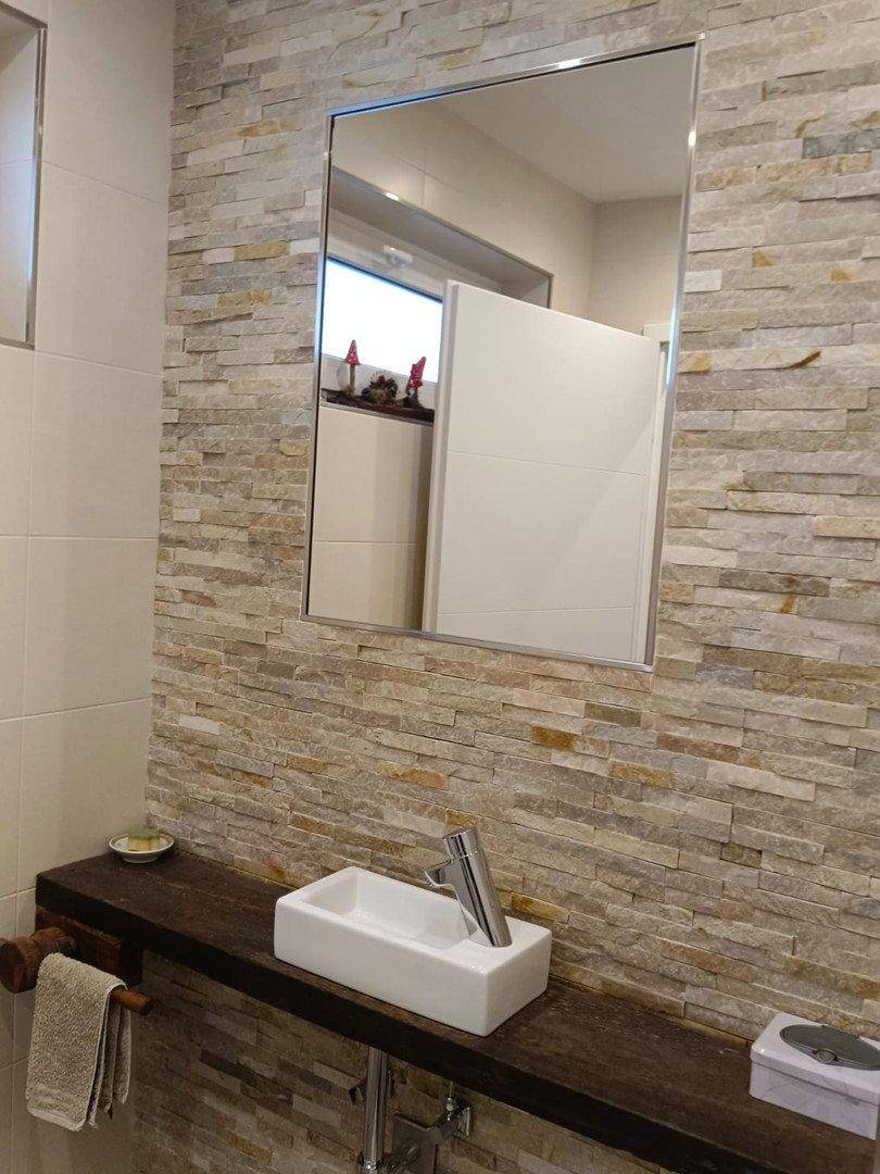 Modernes Gäste-WC mit Steinwand, Aufsatzwaschbecken und großem Spiegel.