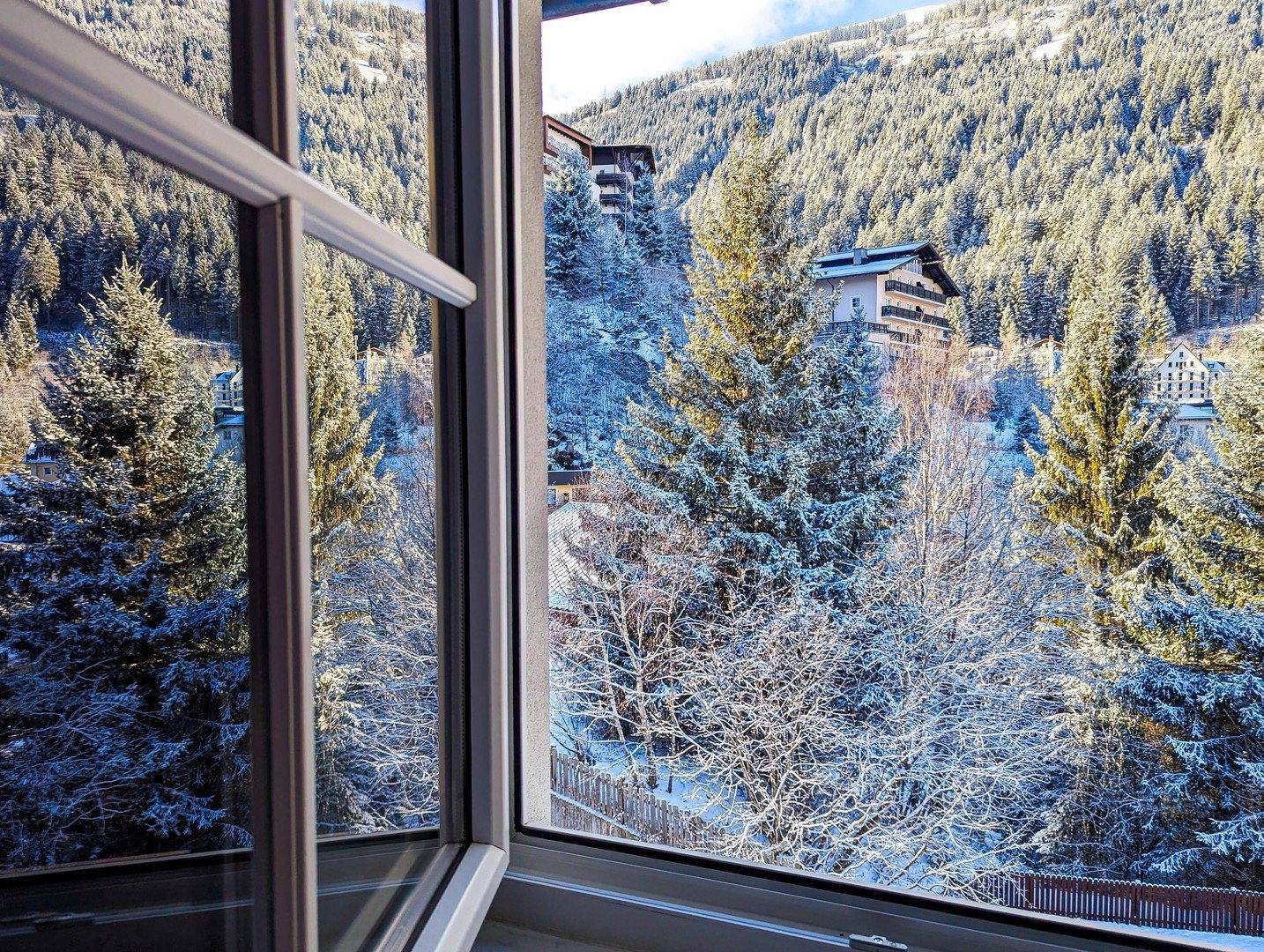 Winterliche Aussicht aus dem Fenster auf verschneite Bäume und ein Gebäude am Hang.