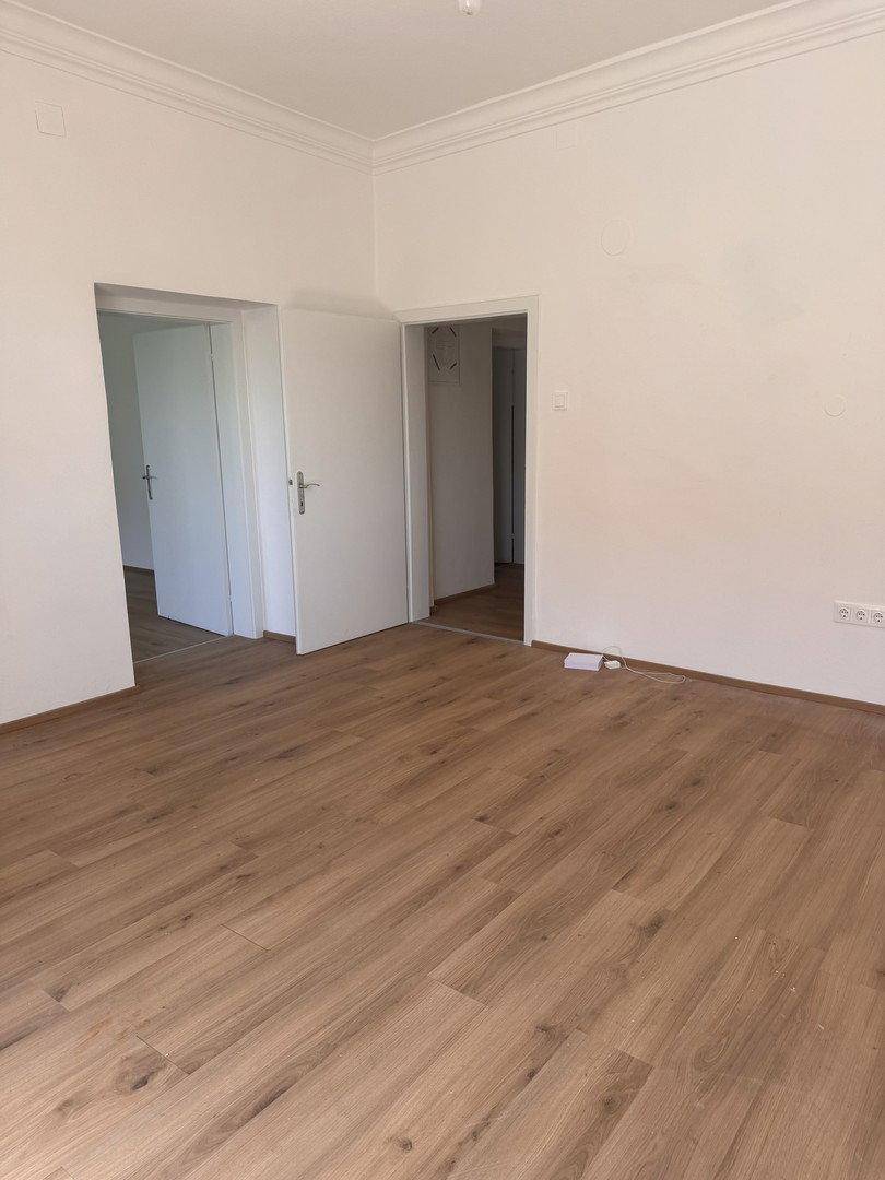 Geräumiger, heller Raum mit Holzboden und zwei Türen, die zu weiteren Zimmern führen.