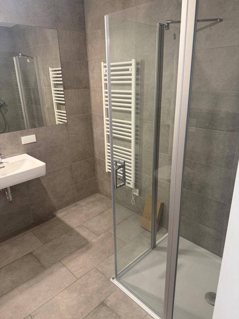 Modernes Badezimmer mit grauen Fliesen, Duschkabine und beheiztem Handtuchhalter.