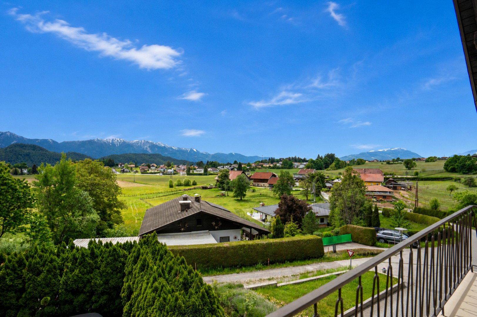 Weitläufiger Panoramablick über das Tal, ein Dorf und die umliegenden Berge von einem Balkon.