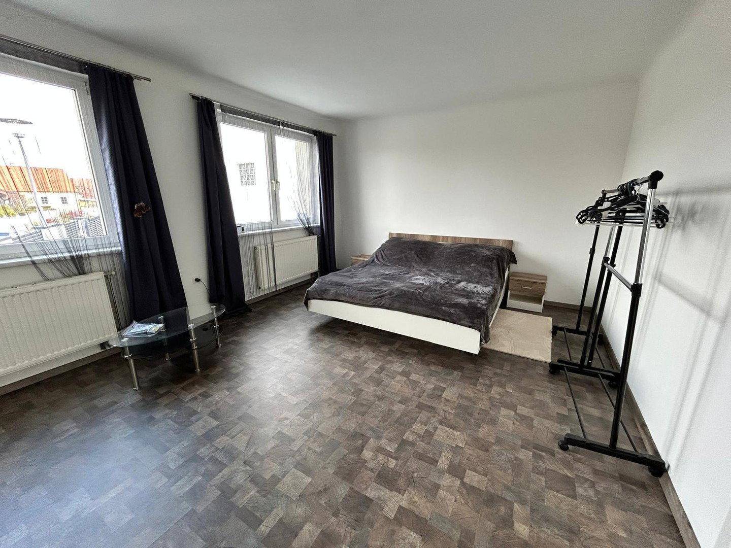 Geräumiges Schlafzimmer mit Doppelbett, zwei Fenstern und dunklem Parkettboden.