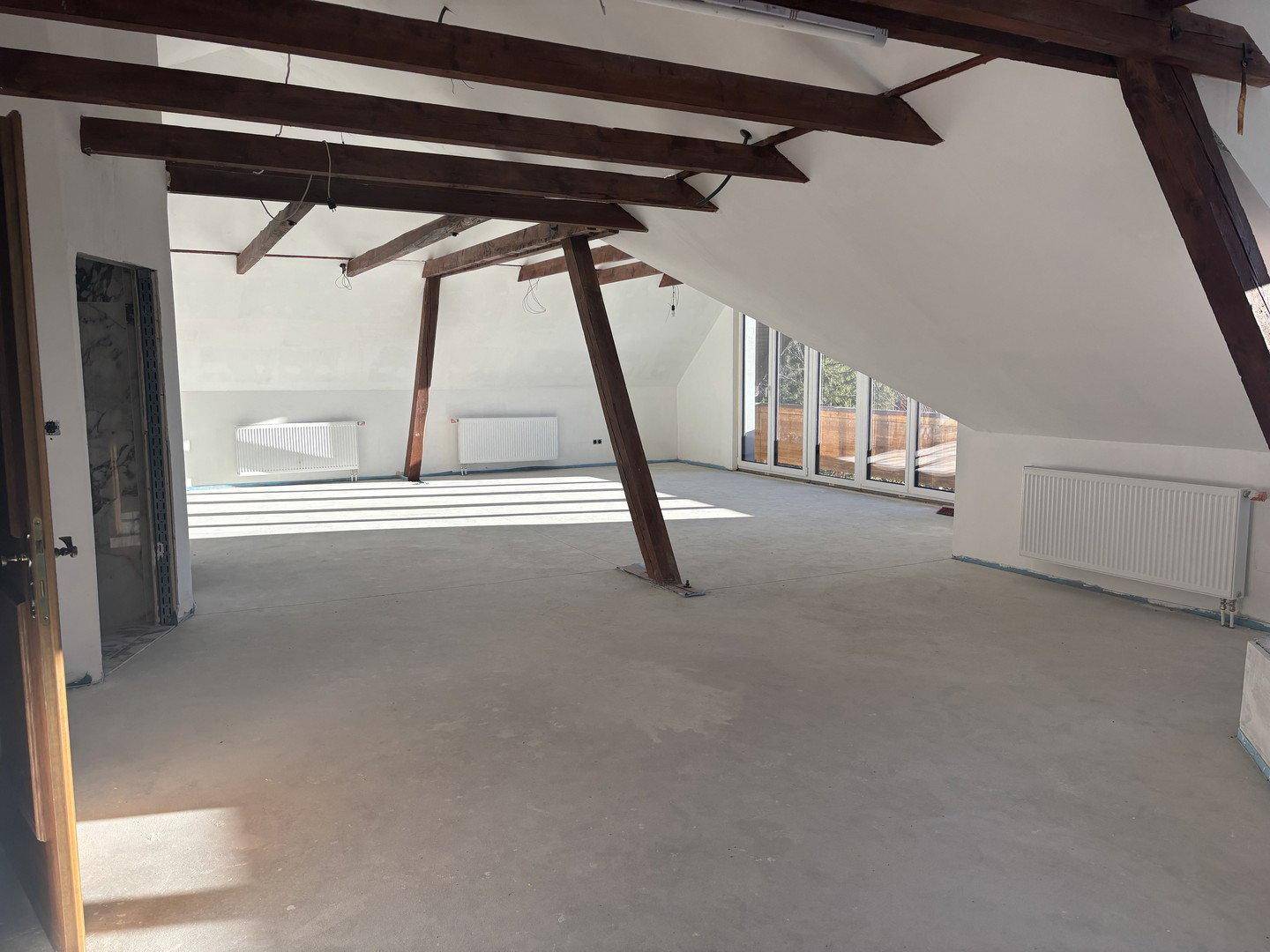 Geräumiger Dachbodenraum mit sichtbaren Holzbalken und Heizkörpern, bereit für den Ausbau.