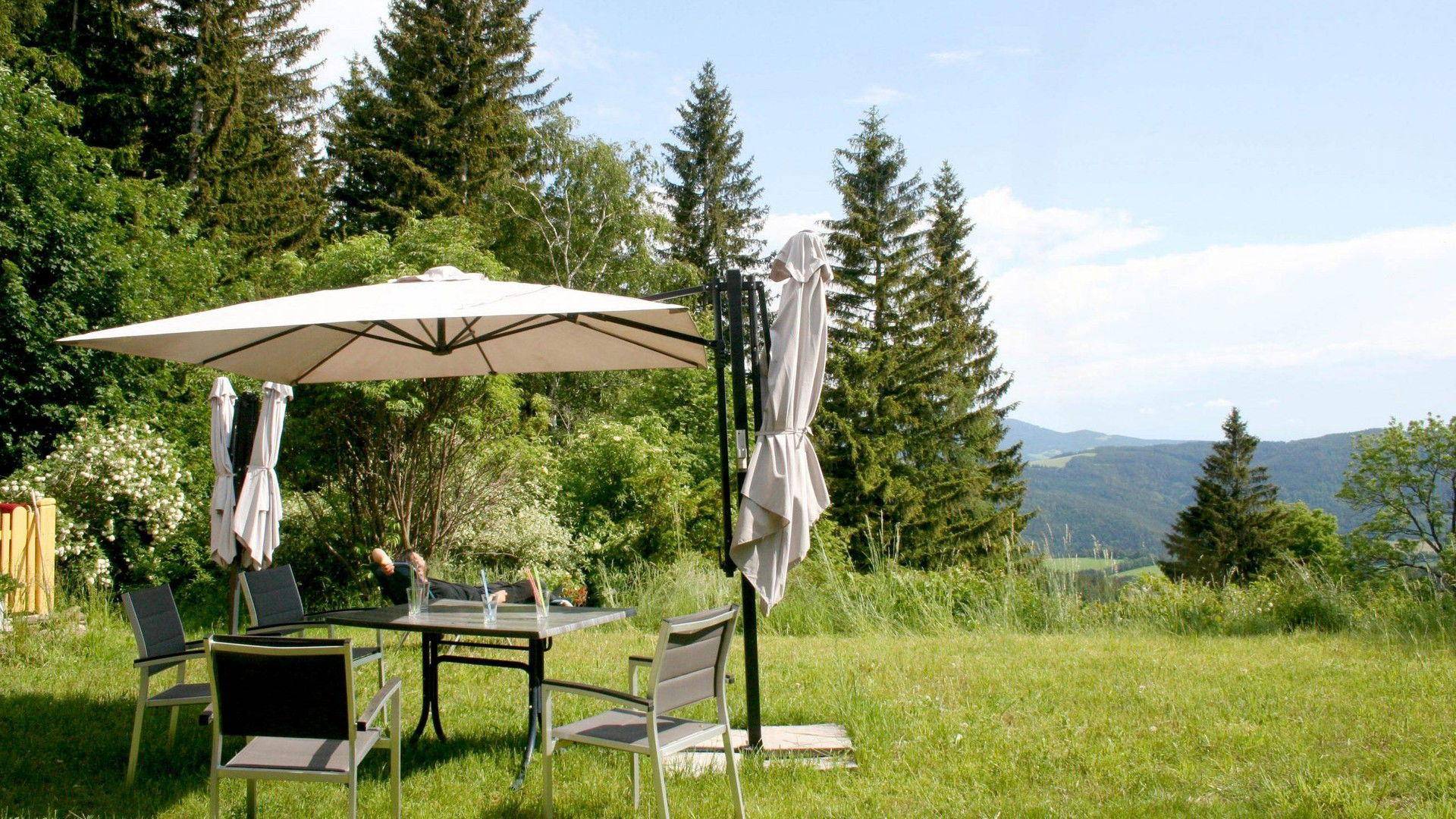 Gemütlicher Sitzbereich im Garten mit Sonnenschirm und Blick auf die grüne Berglandschaft.