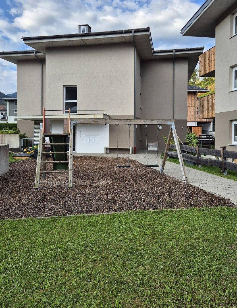 Kinderspielplatz vor einem modernen Gebäude mit Schaukeln und Rutsche.