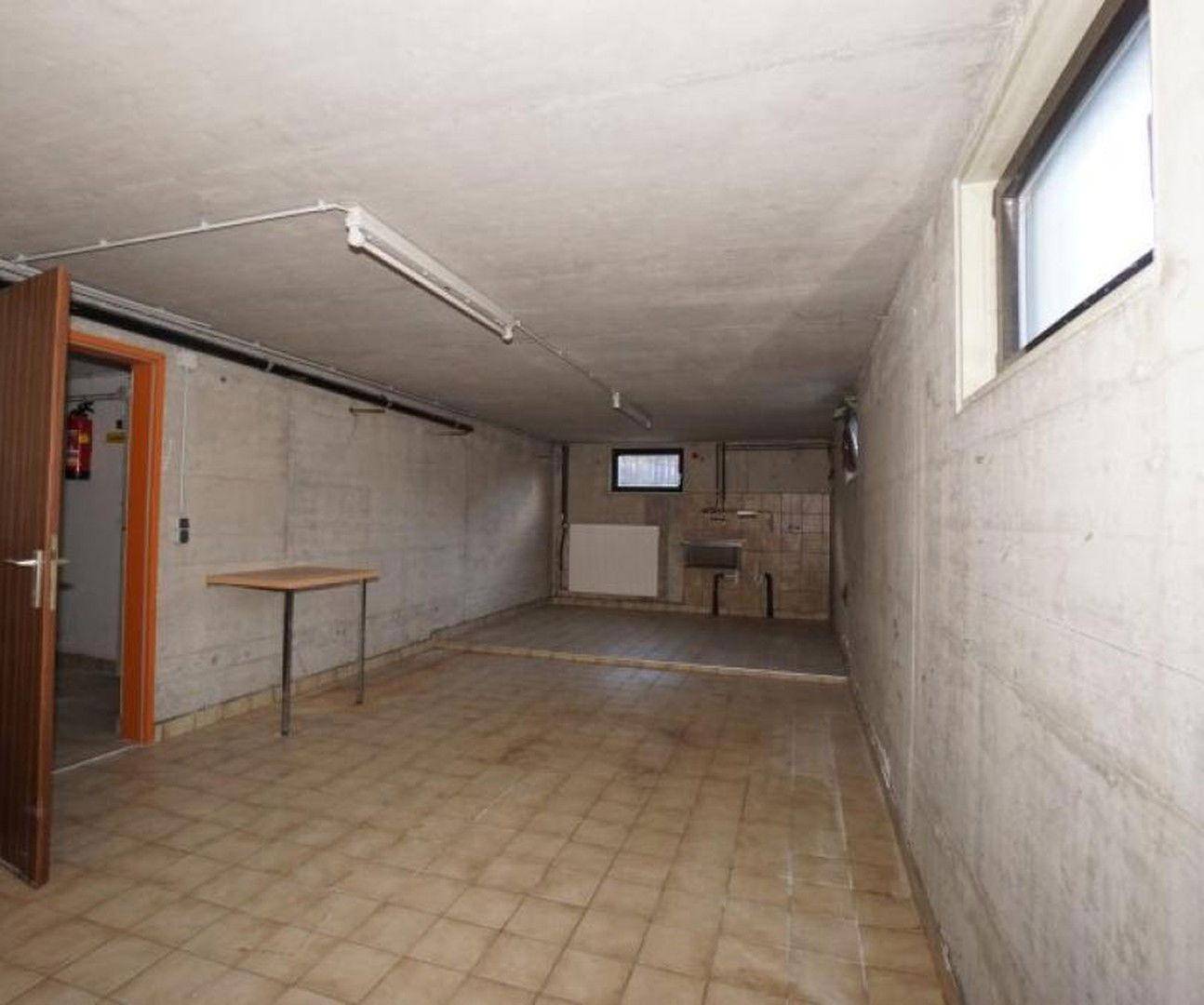 Geräumiger Kellerraum mit Betonwänden, gefliestem Boden und kleinem Fenster.
