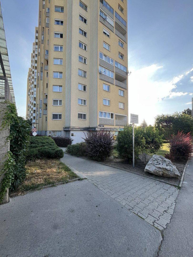 Hohes Wohngebäude mit moderner Architektur, umgeben von Grünflächen und einem gepflasterten Weg.