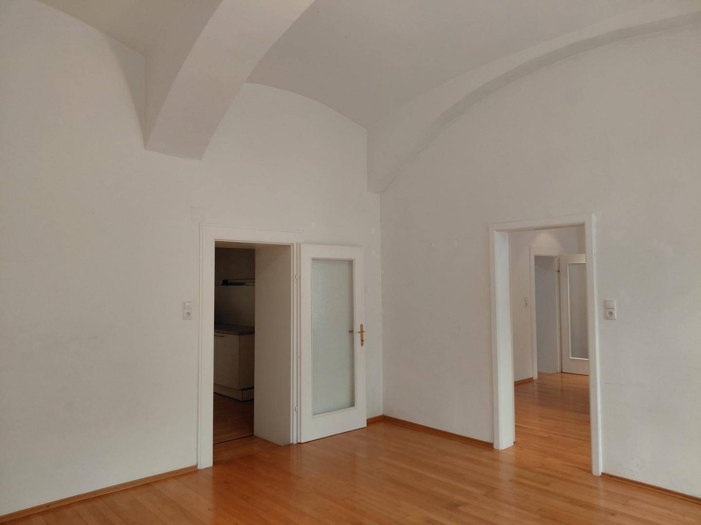 Geräumiger Raum mit Holzboden, gewölbter Decke und mehreren Türen zu angrenzenden Zimmern.