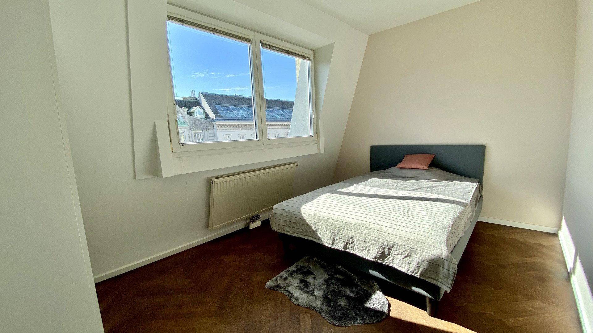 Gemütliches Schlafzimmer mit Holzboden, großem Fenster und schräger Decke.