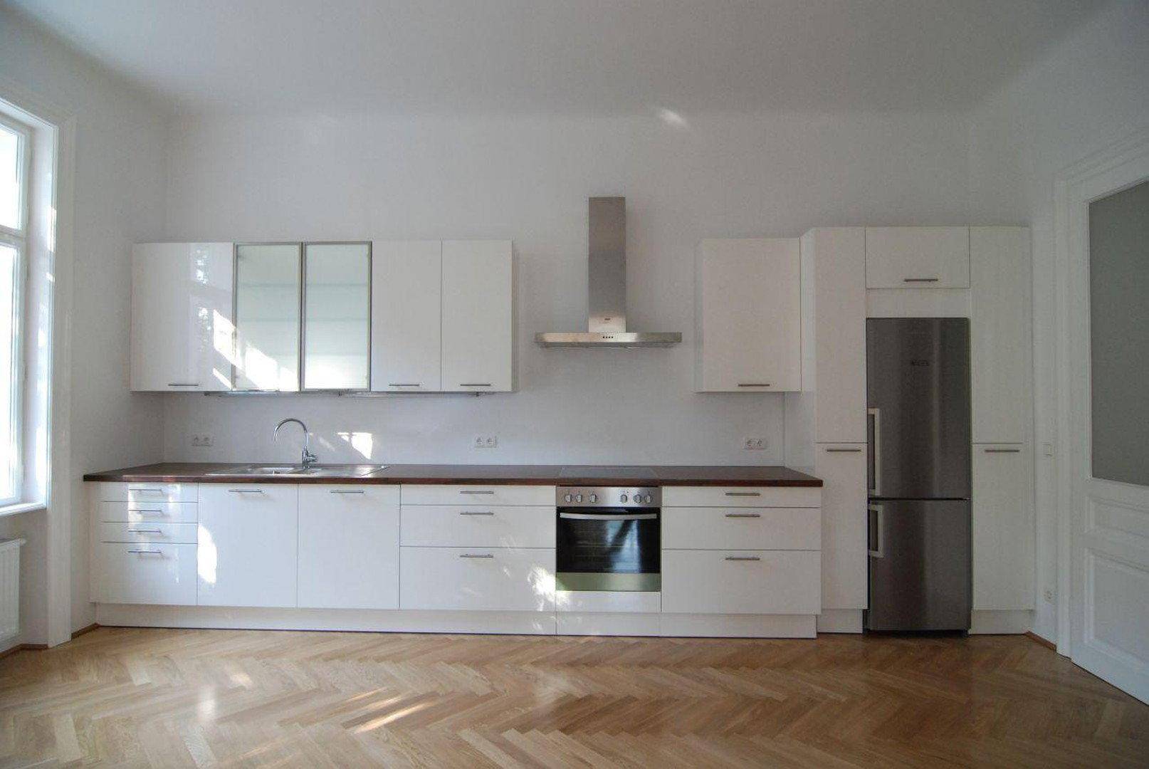 Moderne Einbauküche mit weißen Hochglanzfronten, integriertem Kühlschrank und Fischgrätparkett.