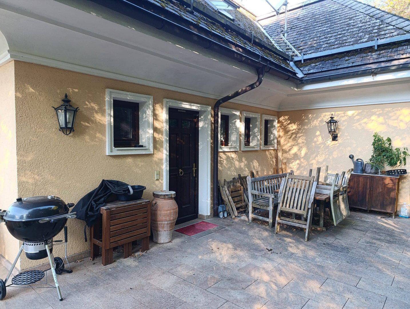 Große gepflasterte Terrasse mit Grillbereich und Gartenmöbeln neben dem Hauseingang.