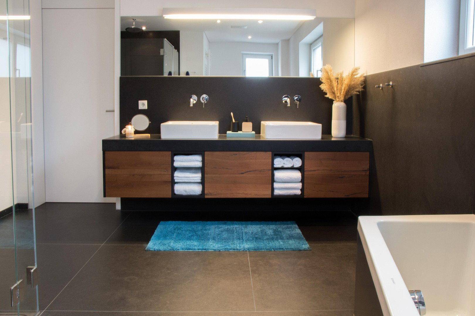 Elegantes modernes Badezimmer mit Doppelwaschbecken, dunklen Fliesen und begehbarer Dusche.