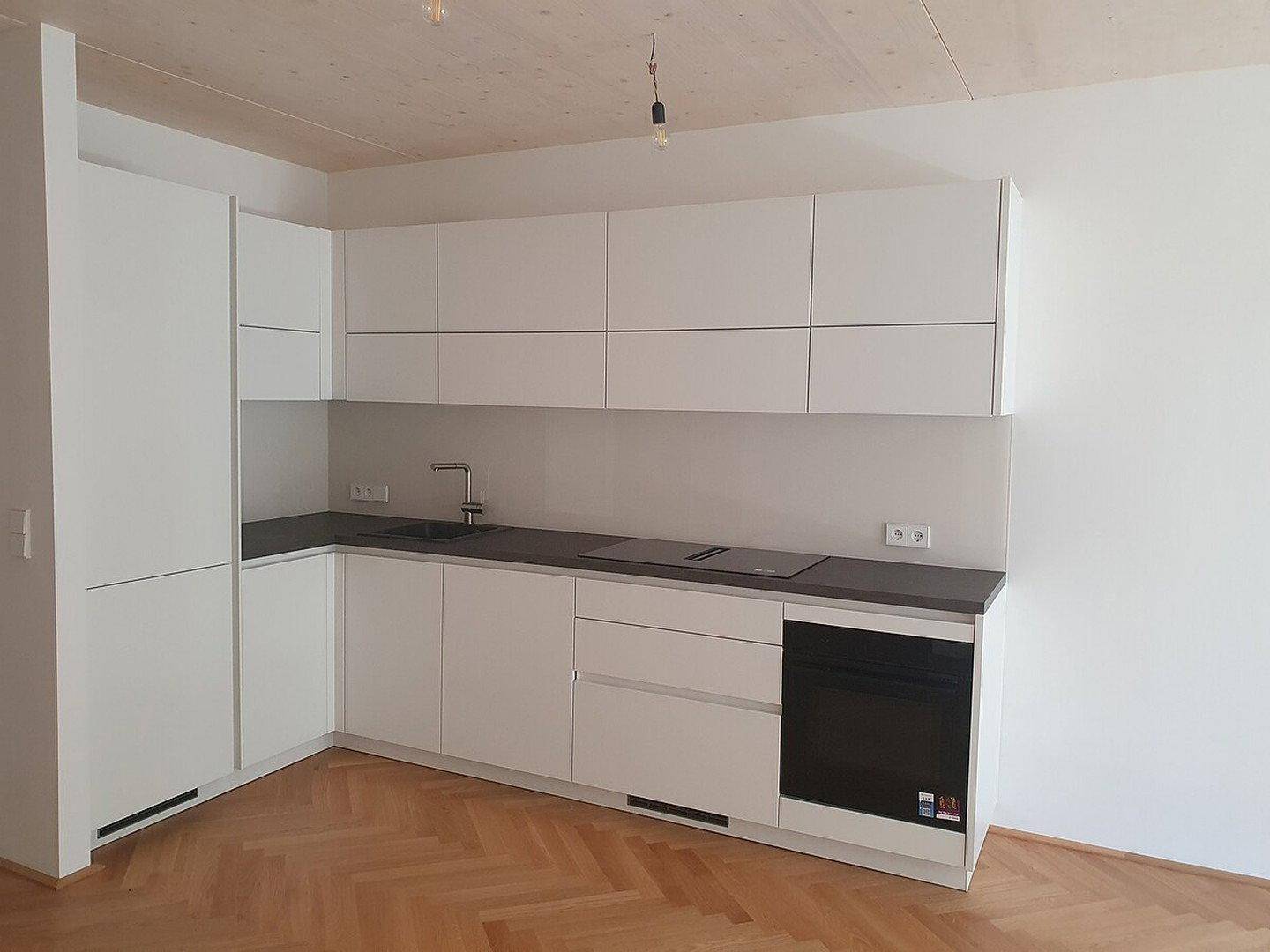 Moderne L-förmige Küche mit weißen Schränken, dunkler Arbeitsplatte und integrierten Geräten.