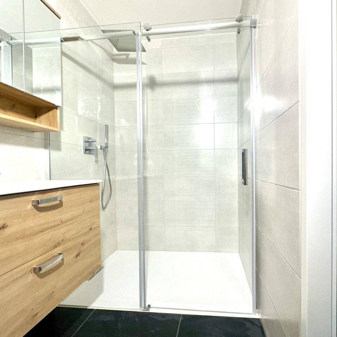 Nahaufnahme der modernen, ebenerdigen Dusche mit Glasabtrennung im Badezimmer.