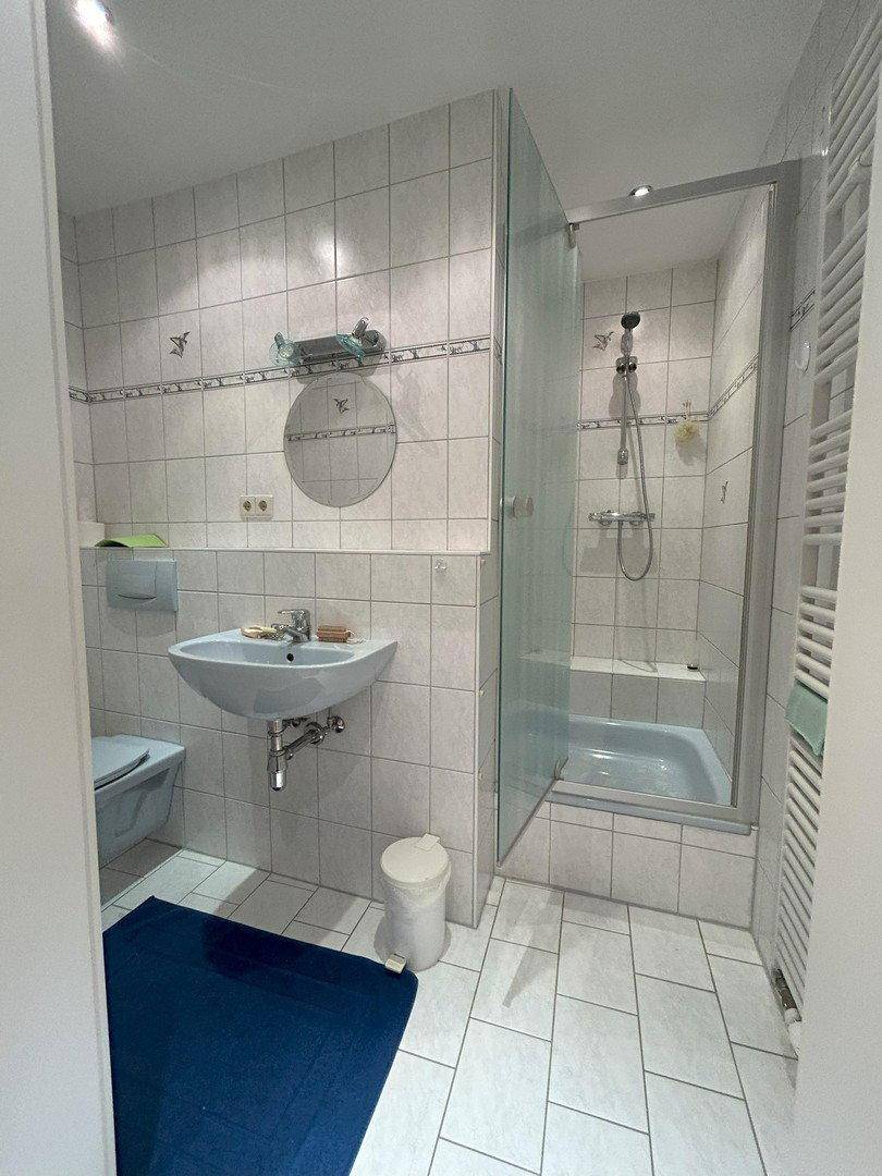 Modernes Badezimmer mit Duschkabine, Waschbecken, WC und hellen Fliesen an Wänden und Boden.