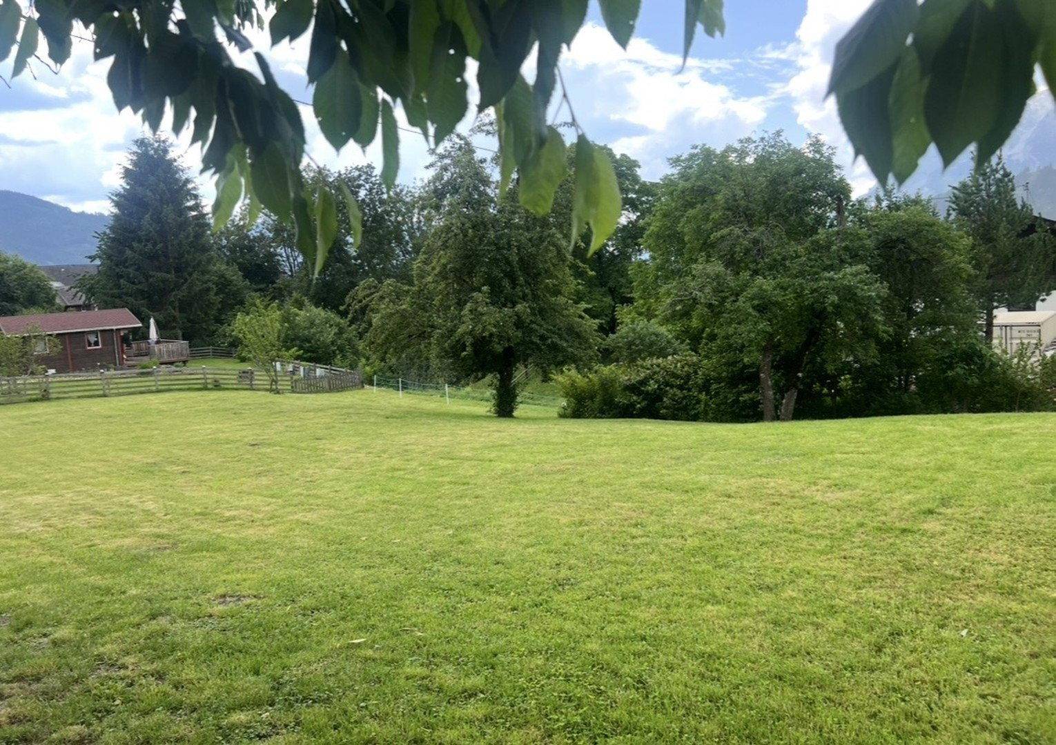 Große grüne Rasenfläche umgeben von Bäumen mit Blick auf die umliegende Landschaft.